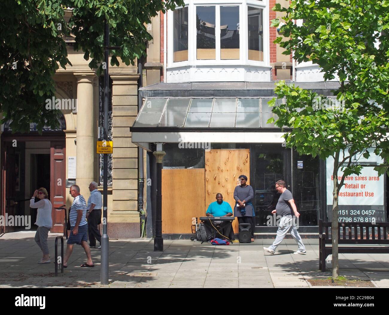 un uomo e una donna che suonano l'organo e cantano fuori da un negozio vuoto su lord street a southport merseyside con persone che camminano p Foto Stock