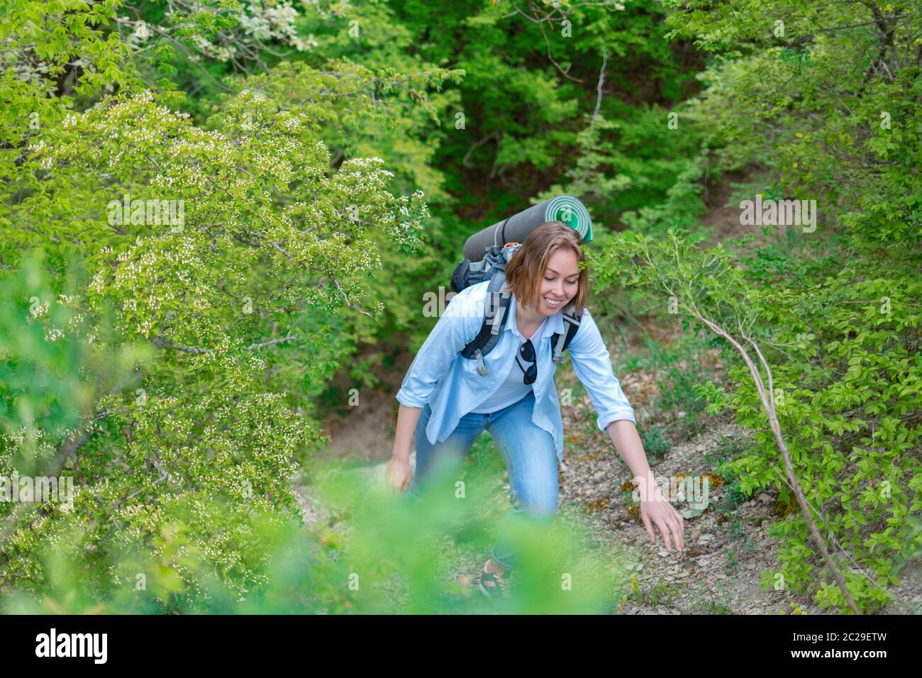 Donna sorridente che sale su un sentiero di montagna. Piante e alberi sullo sfondo. Sport e turismo attivi. Foto Stock