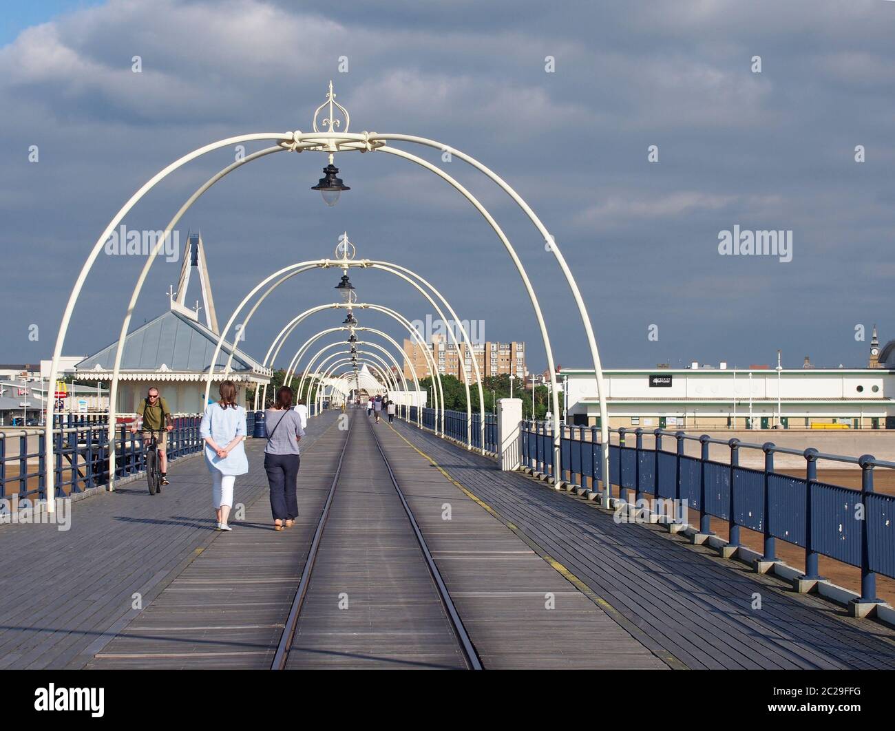 la gente cammina lungo il molo a southport merseyside in una giornata estiva luminosa con edifici della città contro un cielo blu nuvoloso Foto Stock