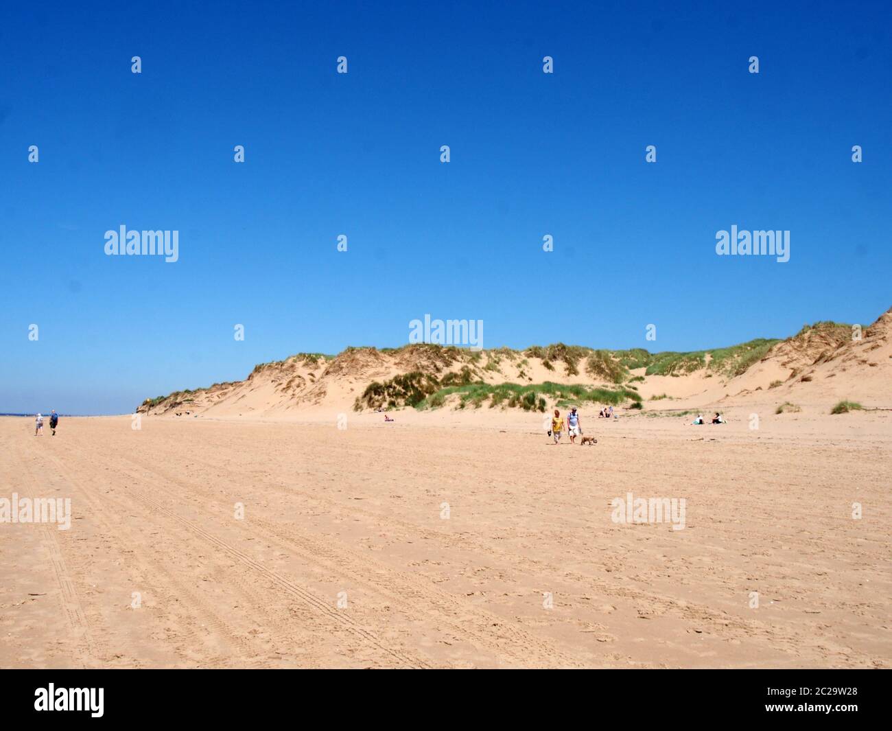 persone che camminano sulla spiaggia con erba sulla cima di alte dune di sabbia sulla costa di sefton a merseyside con blu mare estivo e. Foto Stock