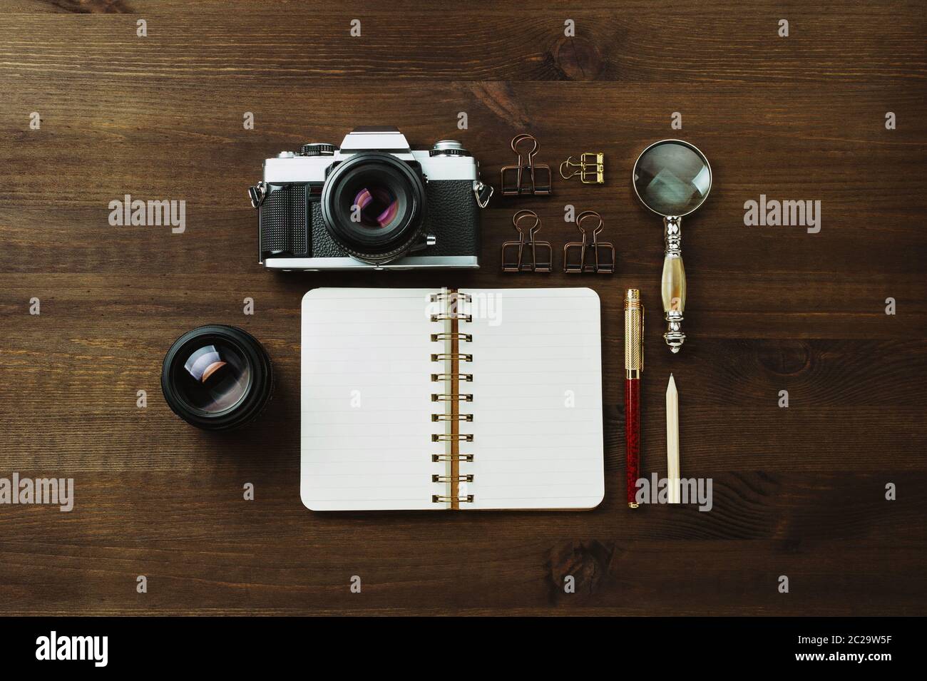 Macchina fotografica con pellicola d'epoca, obiettivi e cancelleria su tavolo di legno scuro, rustica a posa piatta Foto Stock