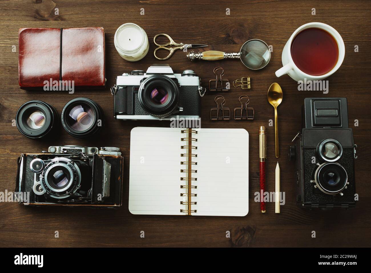 Macchina fotografica con pellicola d'epoca, obiettivi e cancelleria su tavolo di legno scuro, rustica a posa piatta Foto Stock