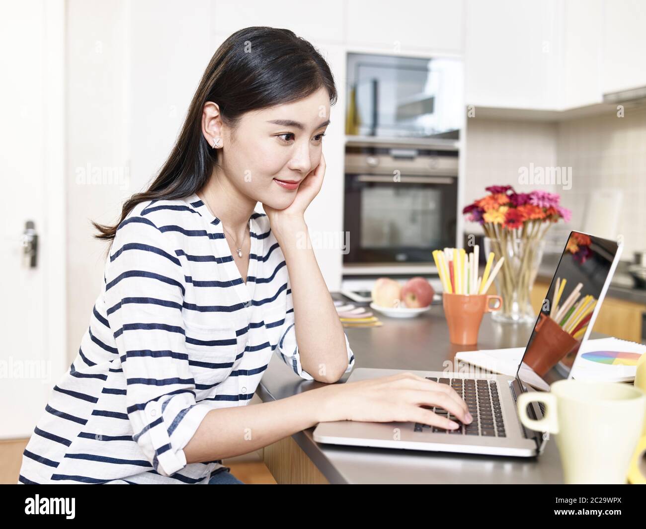 giovane donna d'affari asiatica che lavora da casa seduto al banco della cucina usando il computer portatile Foto Stock
