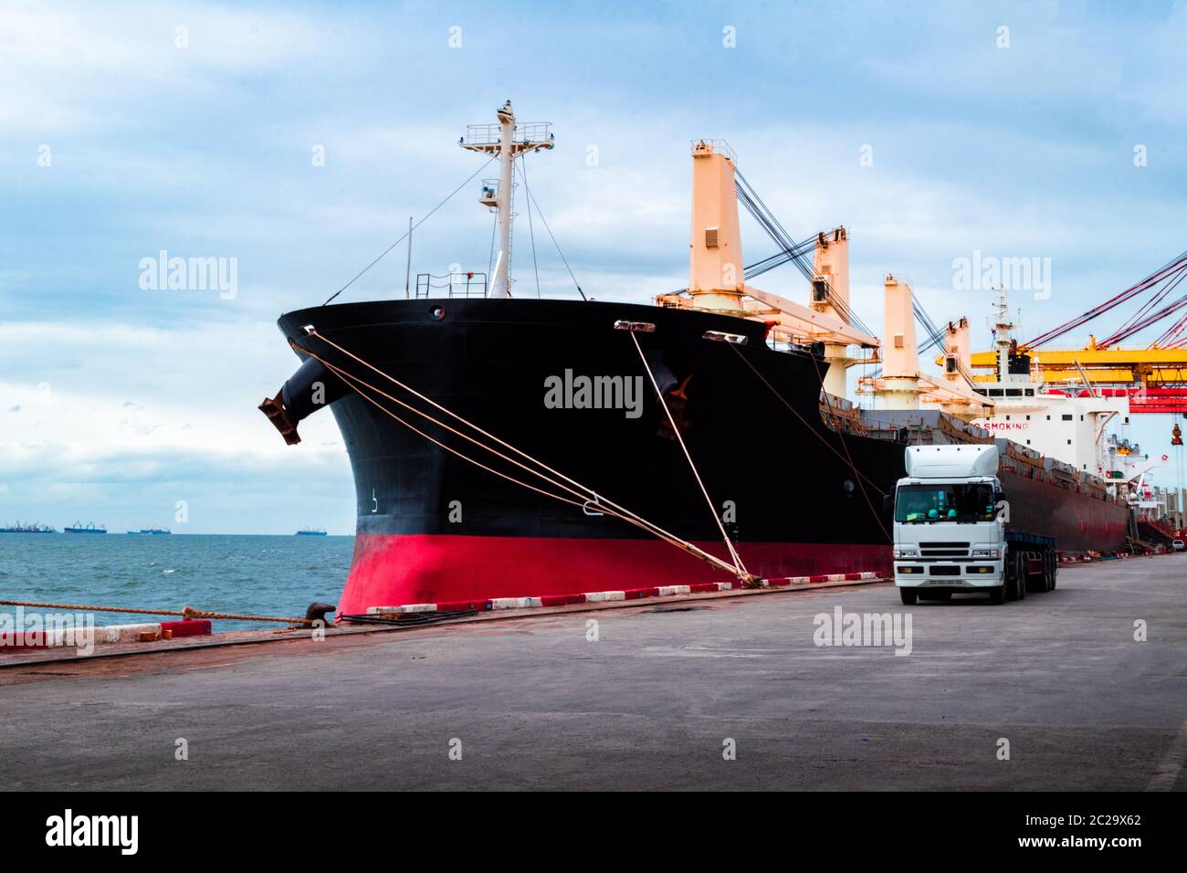 Ormeggio di navi grandi e sfuse al porto che scaricano il carico. Carrello che lascia il terminale dopo il carico. Foto Stock