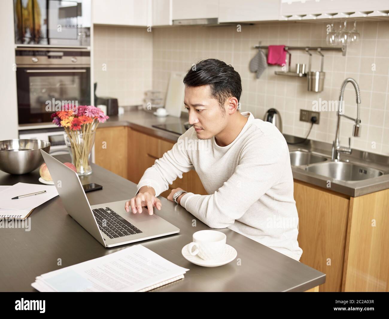 giovane uomo d'affari asiatico seduto cucina contatore che lavora a casa utilizzando computer portatile Foto Stock