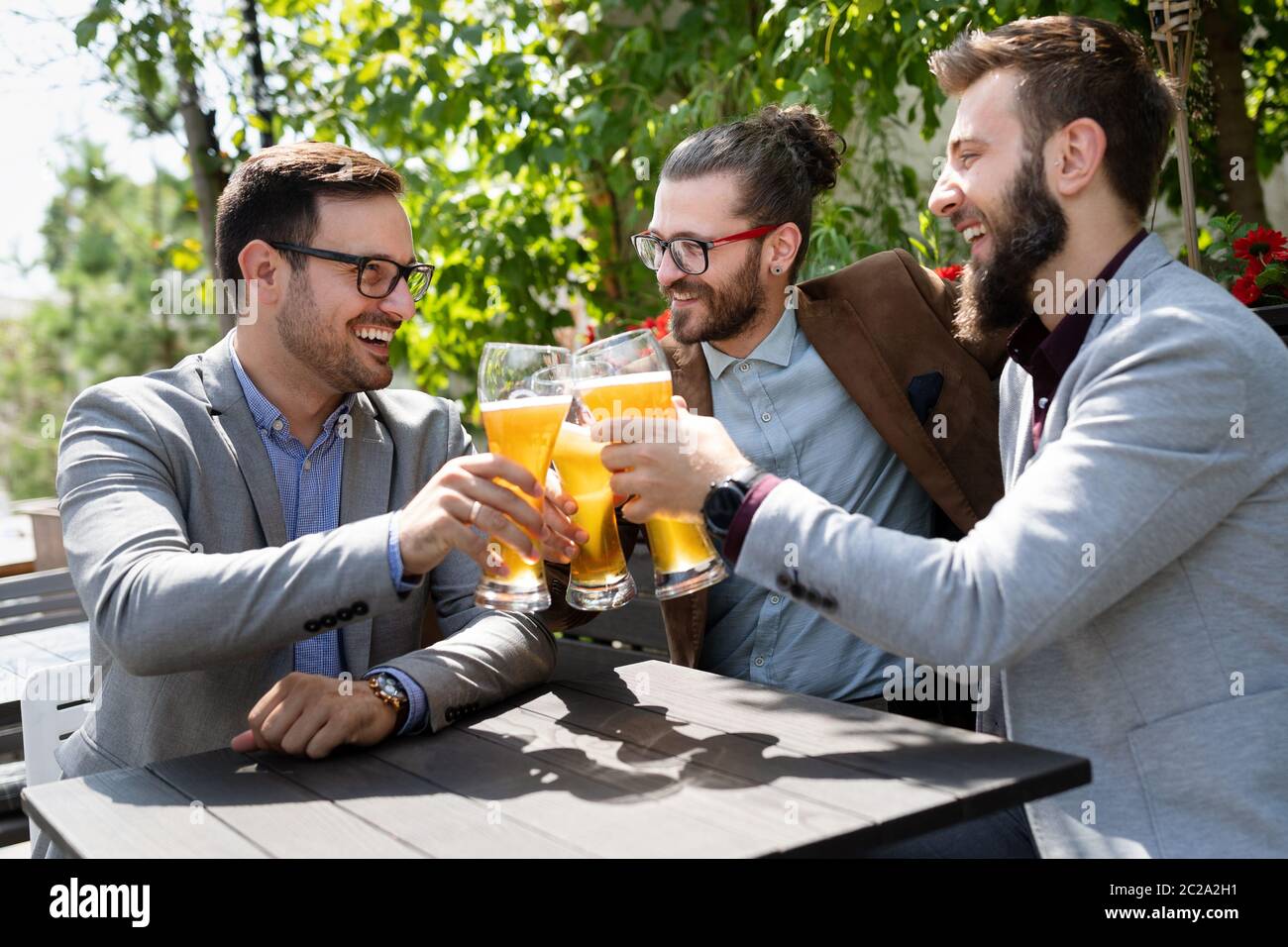 Giovani uomini d'affari bevono birra, parlano e sorridono mentre riposano al pub Foto Stock