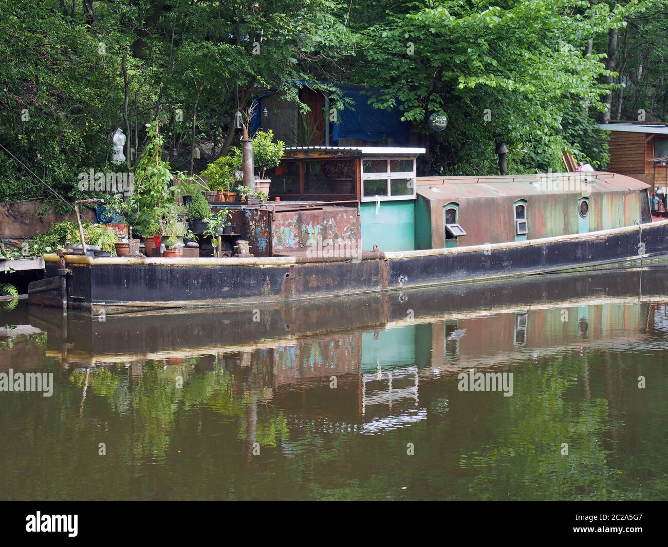 una vecchia barca arrugginita e stretta riflessa nell'acqua e circondata da alberi sul canale rochdale nel ponte di hebden, yorkshire occidentale Foto Stock