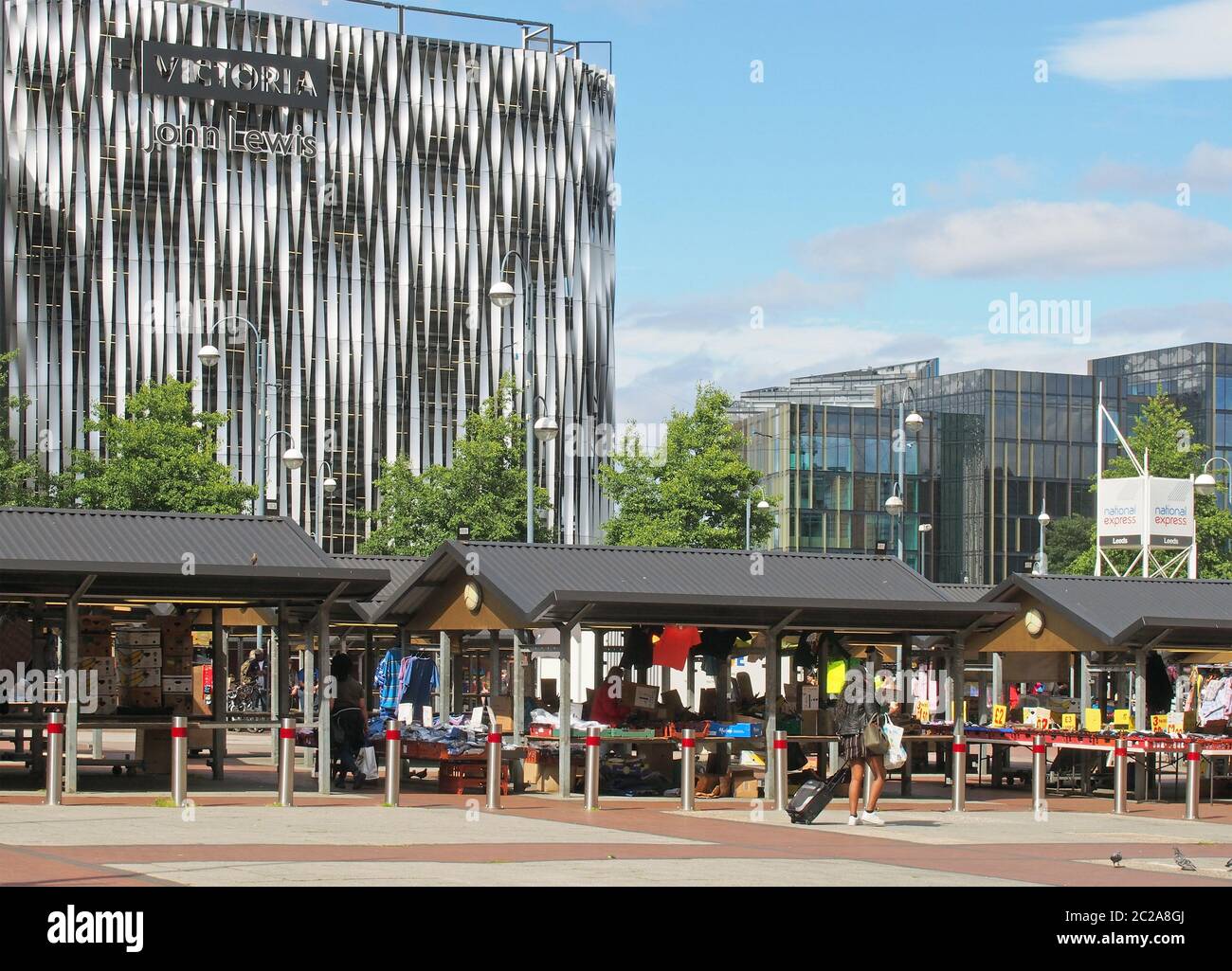 mercato all'aperto di leeds con la gente che acquista presso le bancarelle tradizionali che vendono abbigliamento e cibo di fronte al moderno quartier victoria Foto Stock