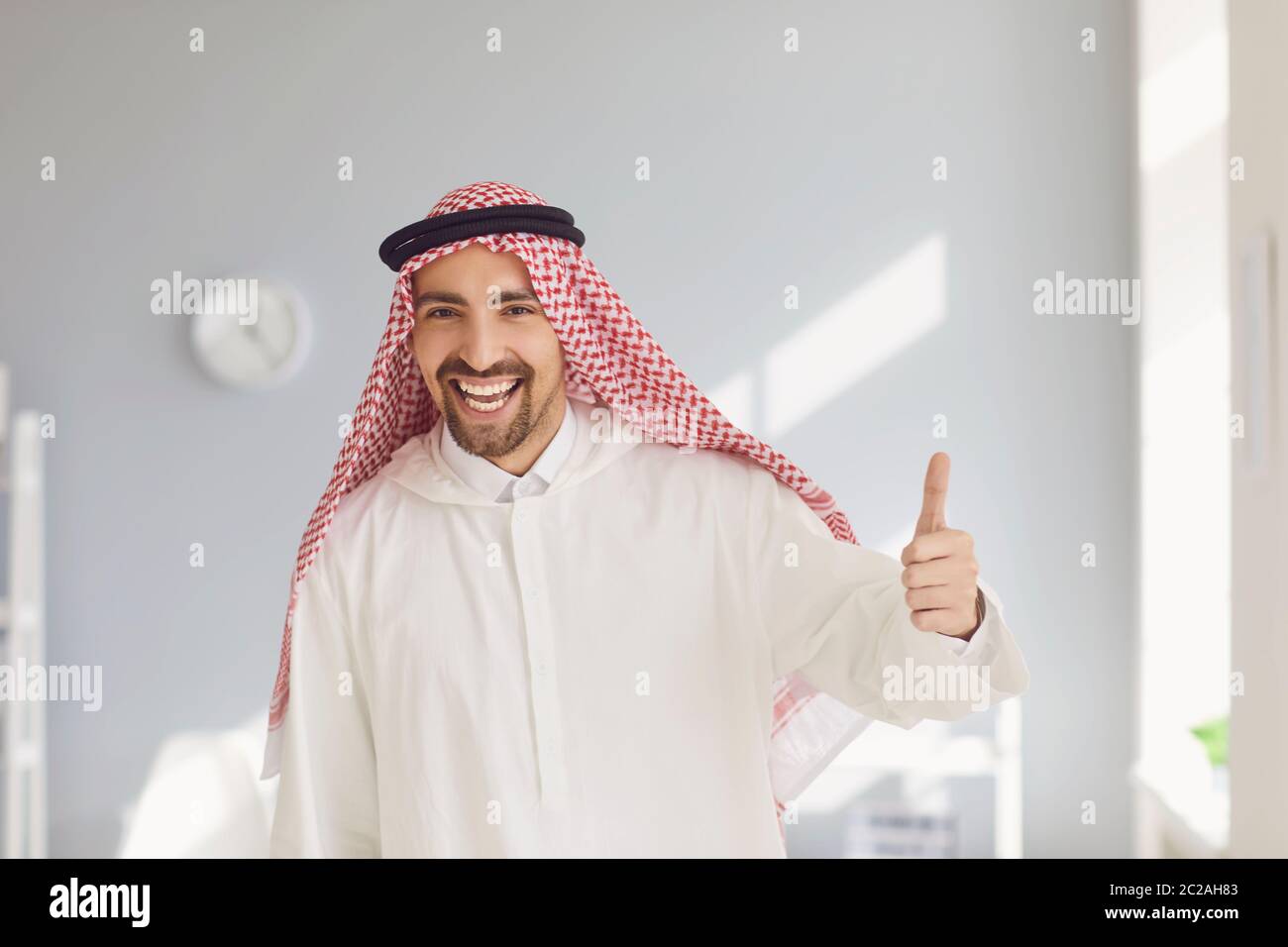 L'uomo arabo felice ha alzato il pollice in un ufficio bianco Foto Stock
