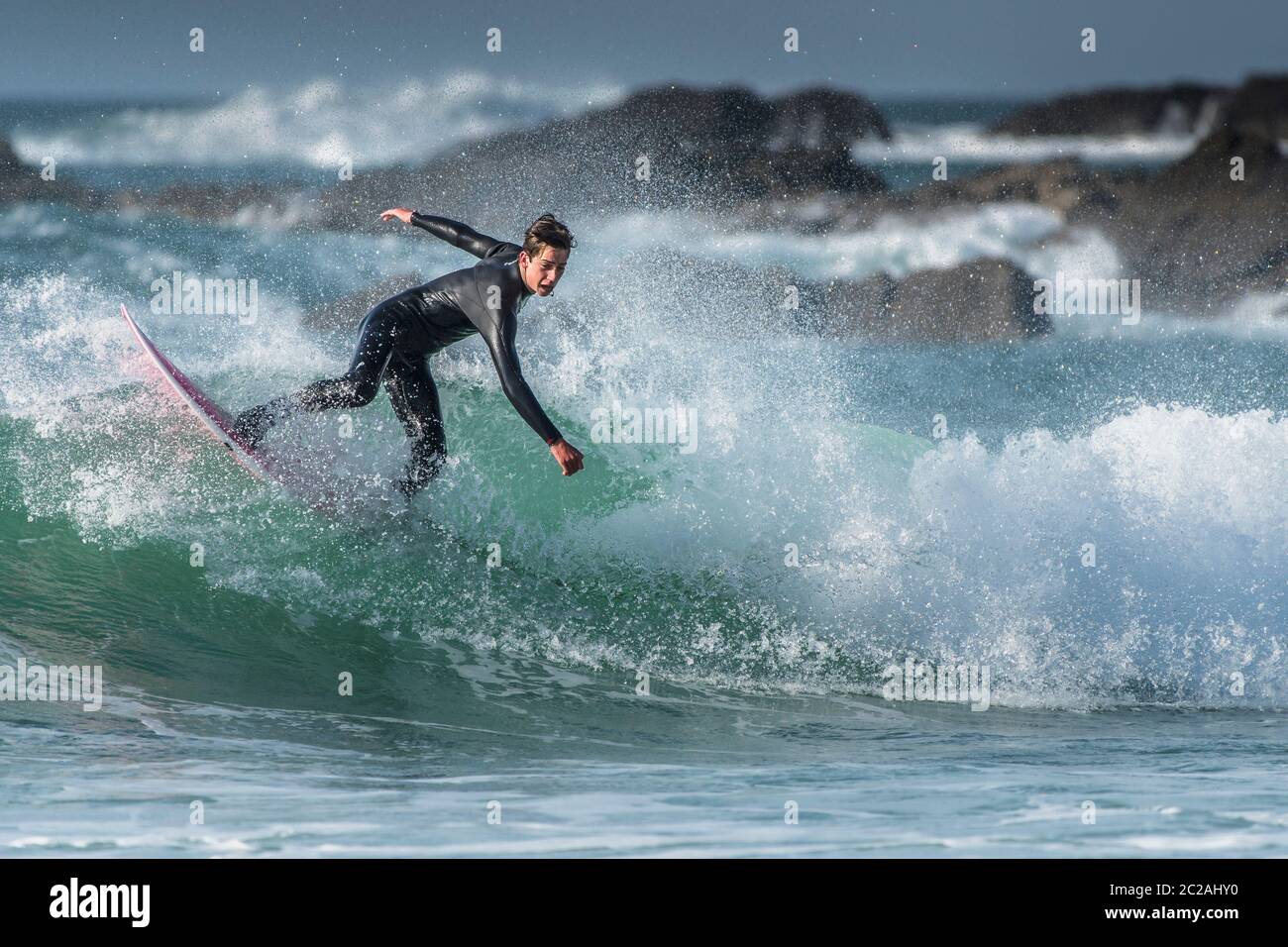 Spettacolare surf azione come un giovane surfista maschio cavalcare un onda a Fistral a Newquay in Cornovaglia. Foto Stock