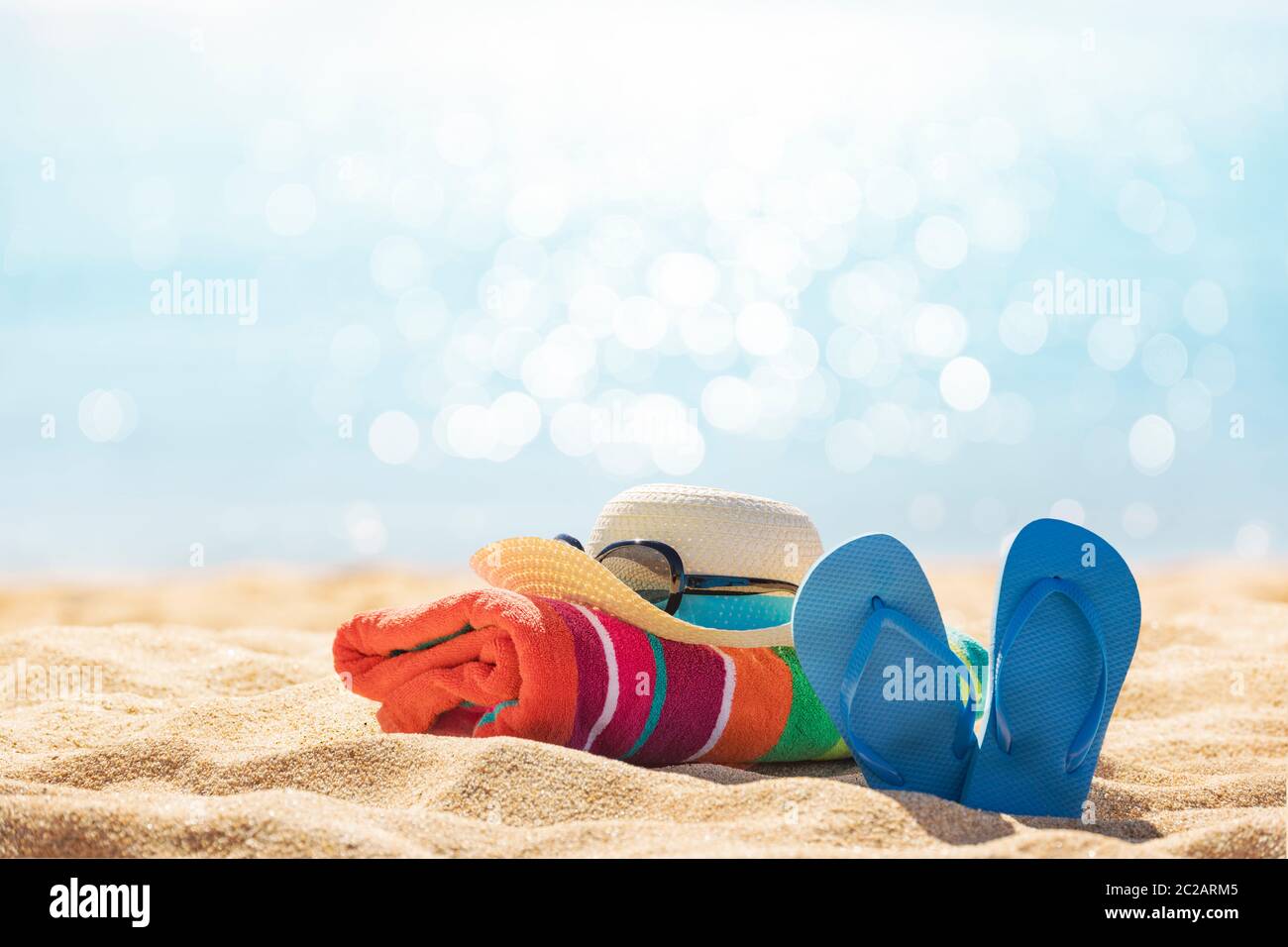 Accessori spiaggia cappello di paglia, infradito, asciugamano sulla soleggiata spiaggia tropicale, vacanze estive Foto Stock