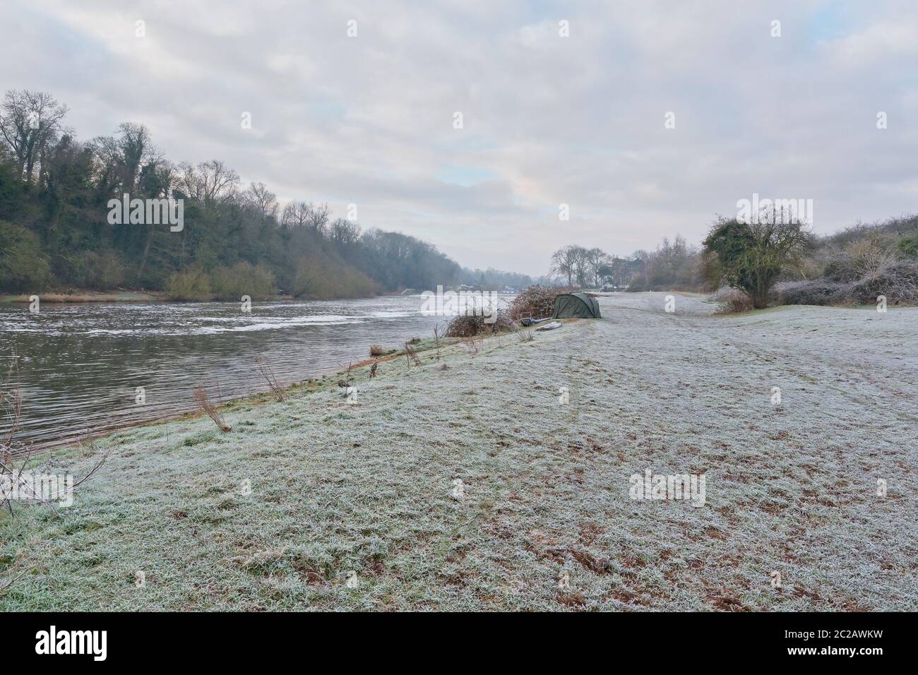 In lontananza una piccola tenda è piantata sulle rive del fiume Trent mentre il gelo si aggrava al terreno Foto Stock