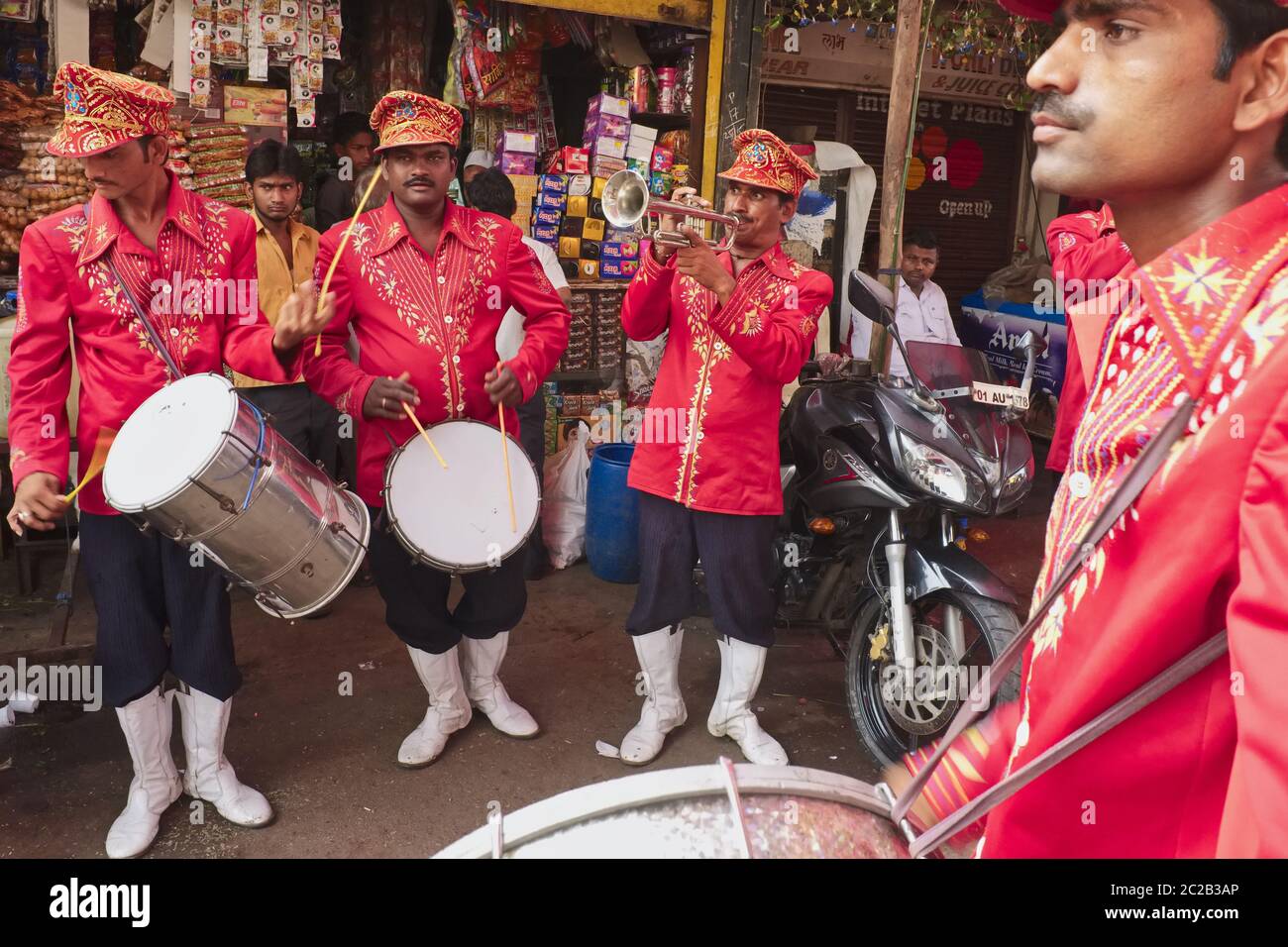 Una band di nozze e festival in uniforme rossa, composta da batteristi e trombettisti, che suonano in una strada a Mumbai, India Foto Stock