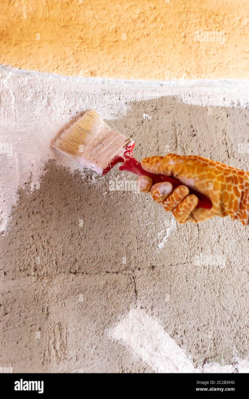 Verniciare una parete di cemento con vernice bianca utilizzando una  spazzola. Guanti gialli con motivo giraffa Foto stock - Alamy