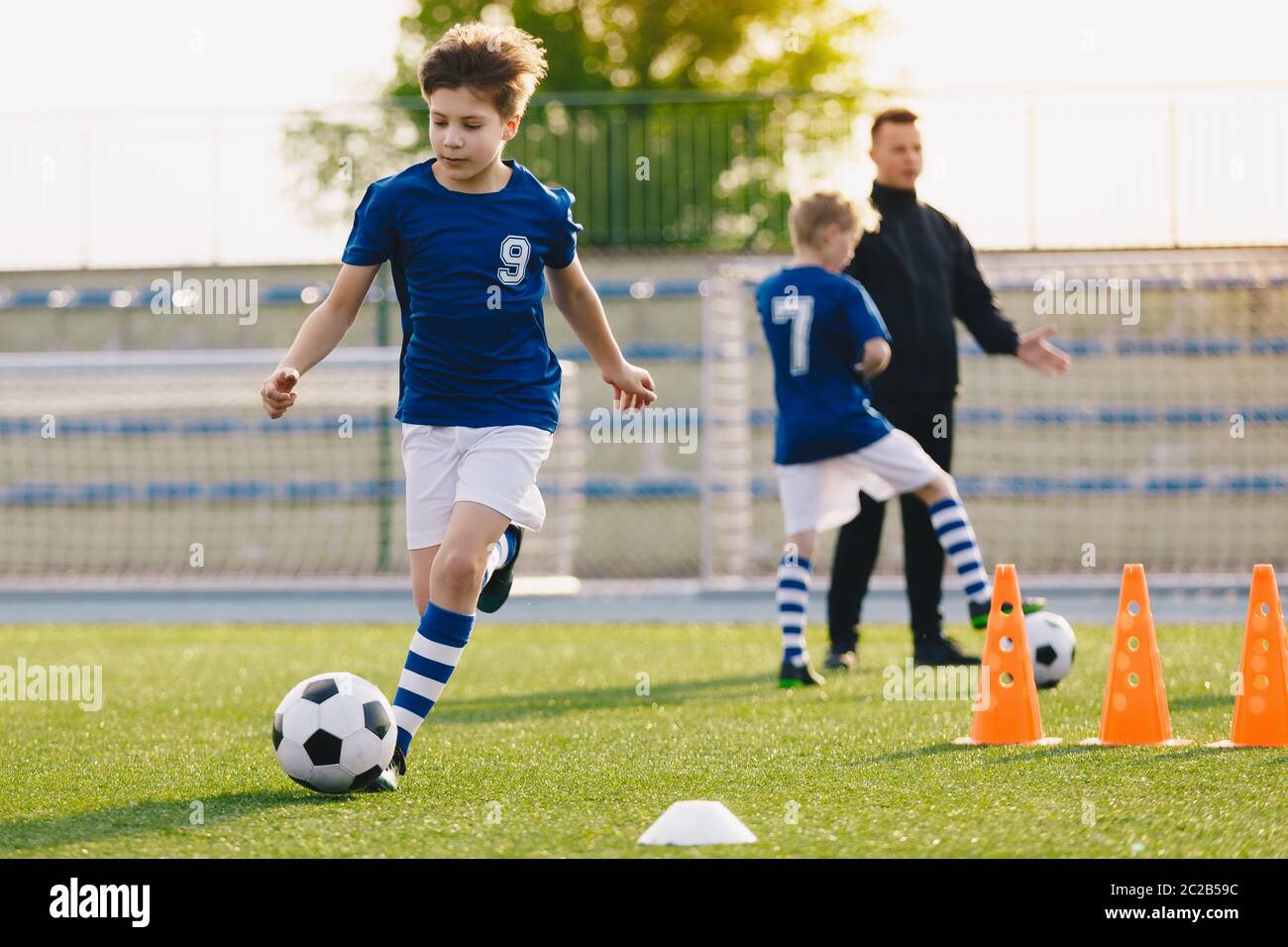 pallone da calcio da corsa ragazzo di 10 anni. Scuola elementare bambini in allenamento di calcio con allenatore giovane. Team sportivo per bambini che migliora la velocità di dribbling Foto Stock