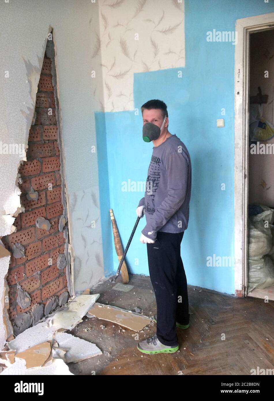 riparazione in casa. Un giovane bussa con iro le lastre di cartongesso dell'epoca sovietica dal muro Foto Stock