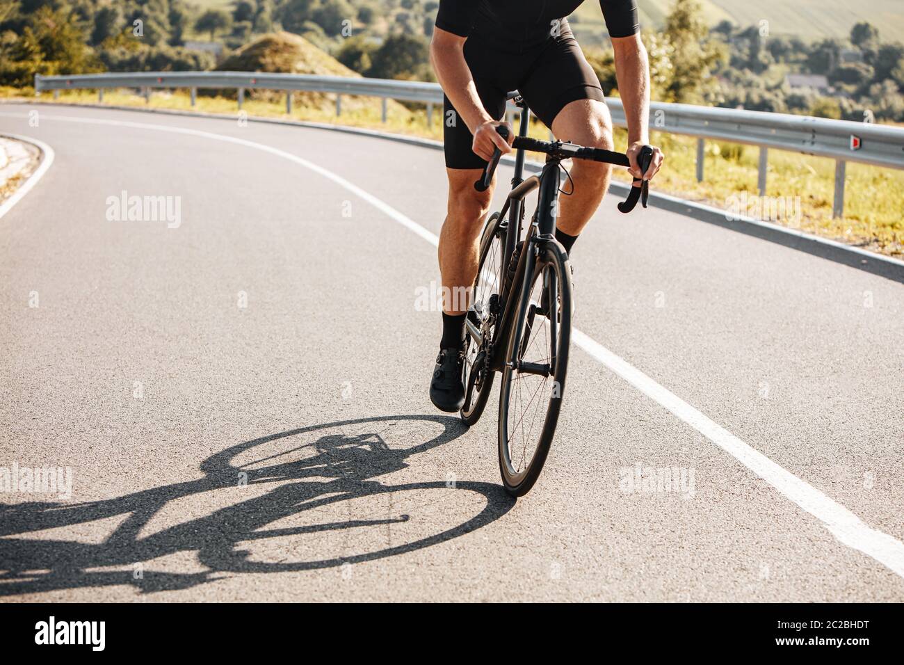 Primo piano di un uomo maturo con corpo resistente che indossa abiti da ciclismo e sneakers, in bicicletta in campagna. Concetto di stile di vita attivo e tra regolare Foto Stock