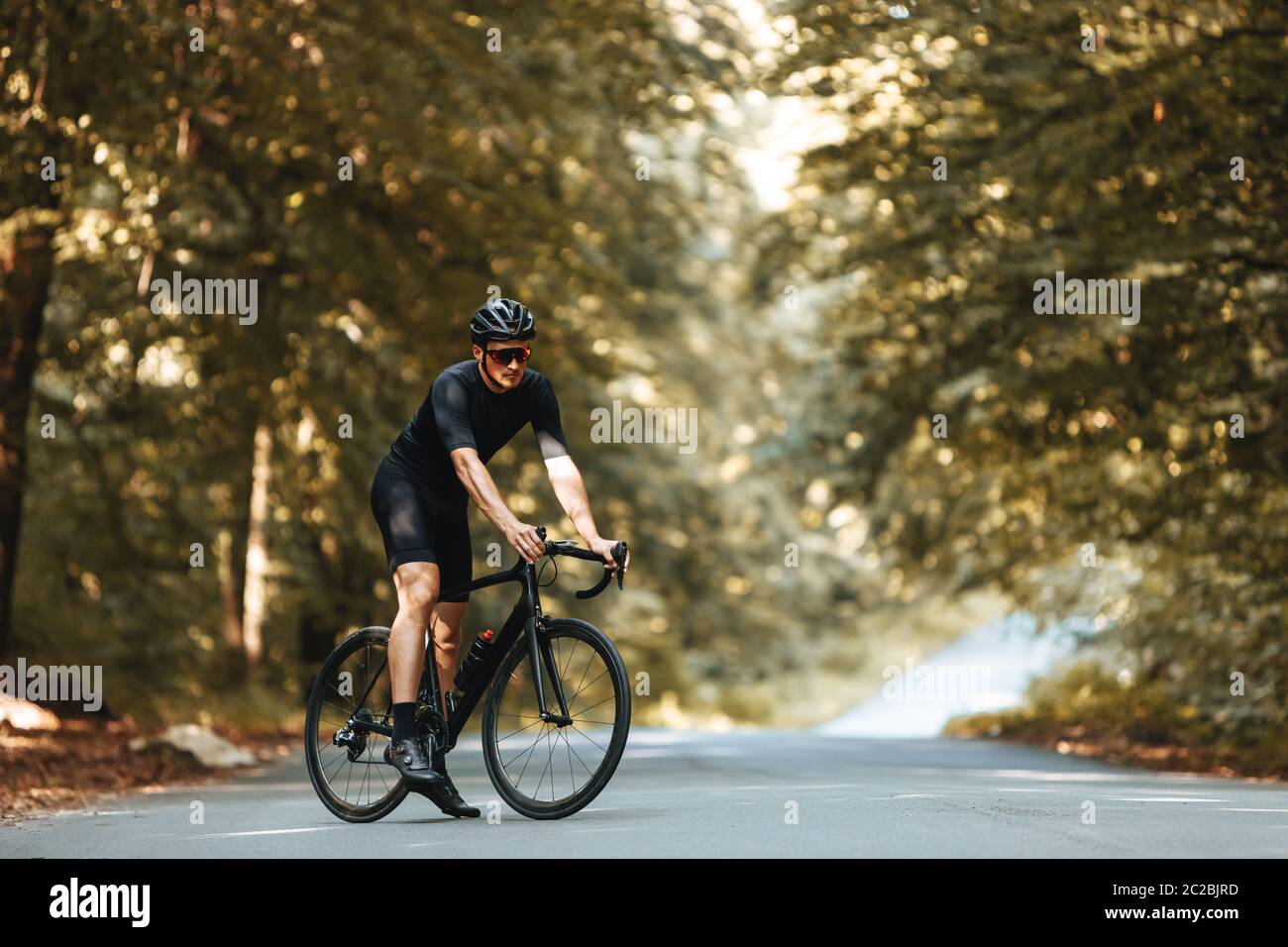Atleta maturo con forma sportiva del corpo vestito in bicicletta, casco e occhiali in piedi con la bicicletta nella foresta estiva. Uomo bearded che si diverta Foto Stock