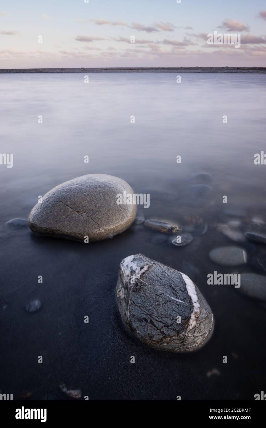 Lunga esposizione di pietre nell'acqua a Okarito sulla costa occidentale dell'isola meridionale della Nuova Zelanda. Foto Stock