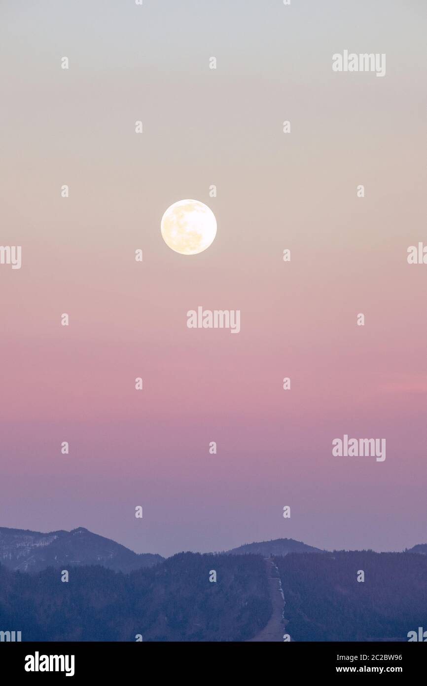 Luna piena sopra le montagne. Cielo rosa, viola con luna grande. Foto Stock