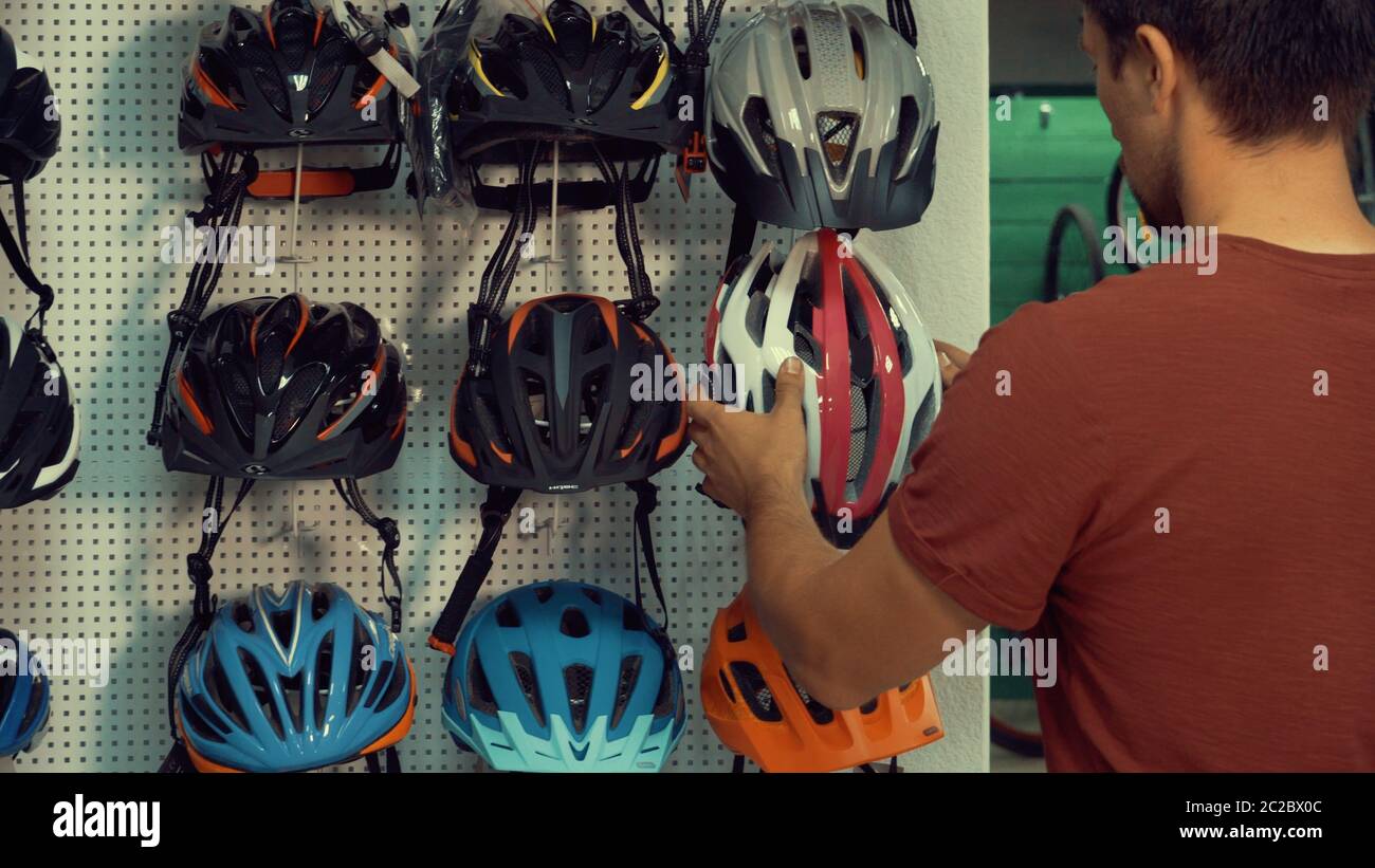 Un giovane caucasico si trova vicino a un stand in un negozio di biciclette nel reparto protezione testa. Scegliere un casco da bicicletta in un s. Foto Stock
