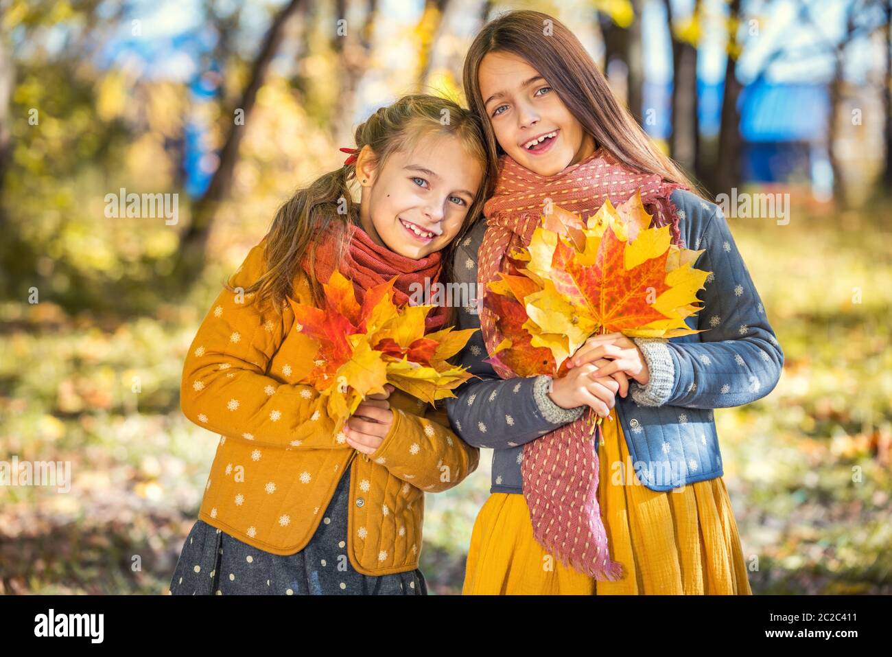 Due ragazze sorridenti e carine di 8 anni che si posano insieme in un parco in una giornata di sole autunno. Concetto di amicizia. Foto Stock