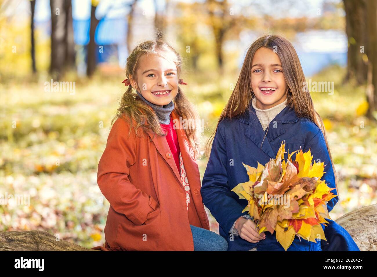 Due ragazze sorridenti e carine di 8 anni che si posano insieme in un parco in una giornata di sole autunno. Concetto di amicizia. Foto Stock