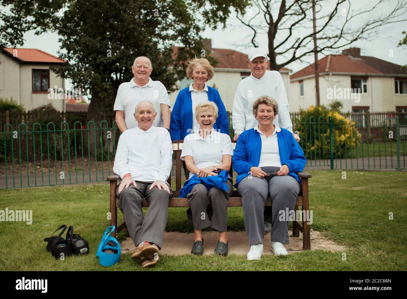 Un gruppo di anziani adulti seduti su una panchina a bowling green, guardando la telecamera. Foto Stock