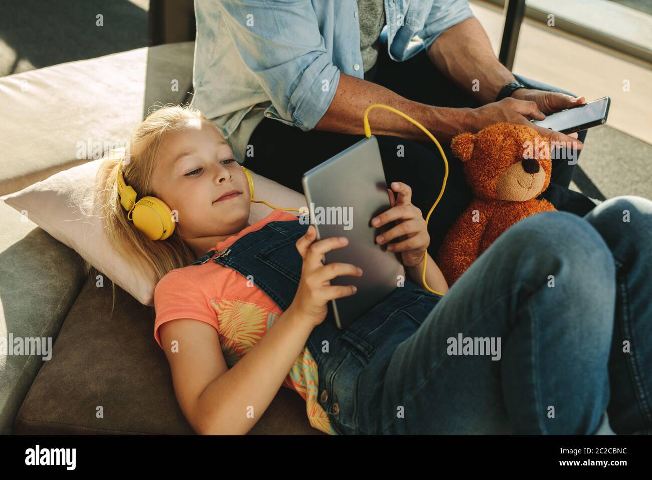 Ragazza che usa un tablet pc con il padre seduto di fianco a un telefono cellulare nella sala d'attesa dell'aeroporto. Famiglia relax presso la sala d'attesa aeroporto. Foto Stock