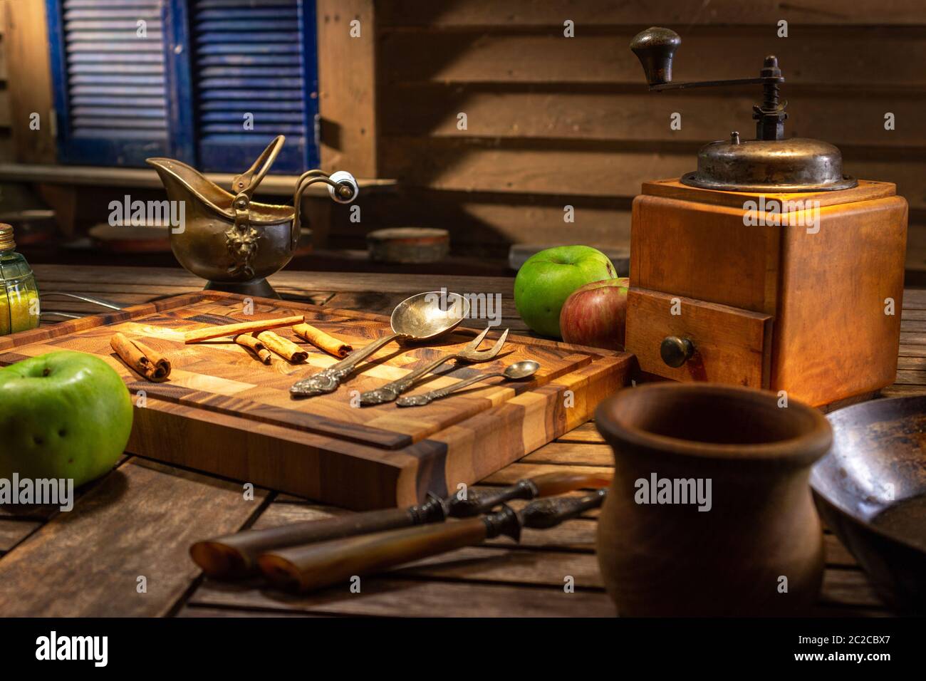 Vintage ancora vita con piatti antichi e mele verdi. Macinacaffè nostalgico su vecchio tavolo e fondo di legno testurizzato. Illuminazione cinematografica Foto Stock