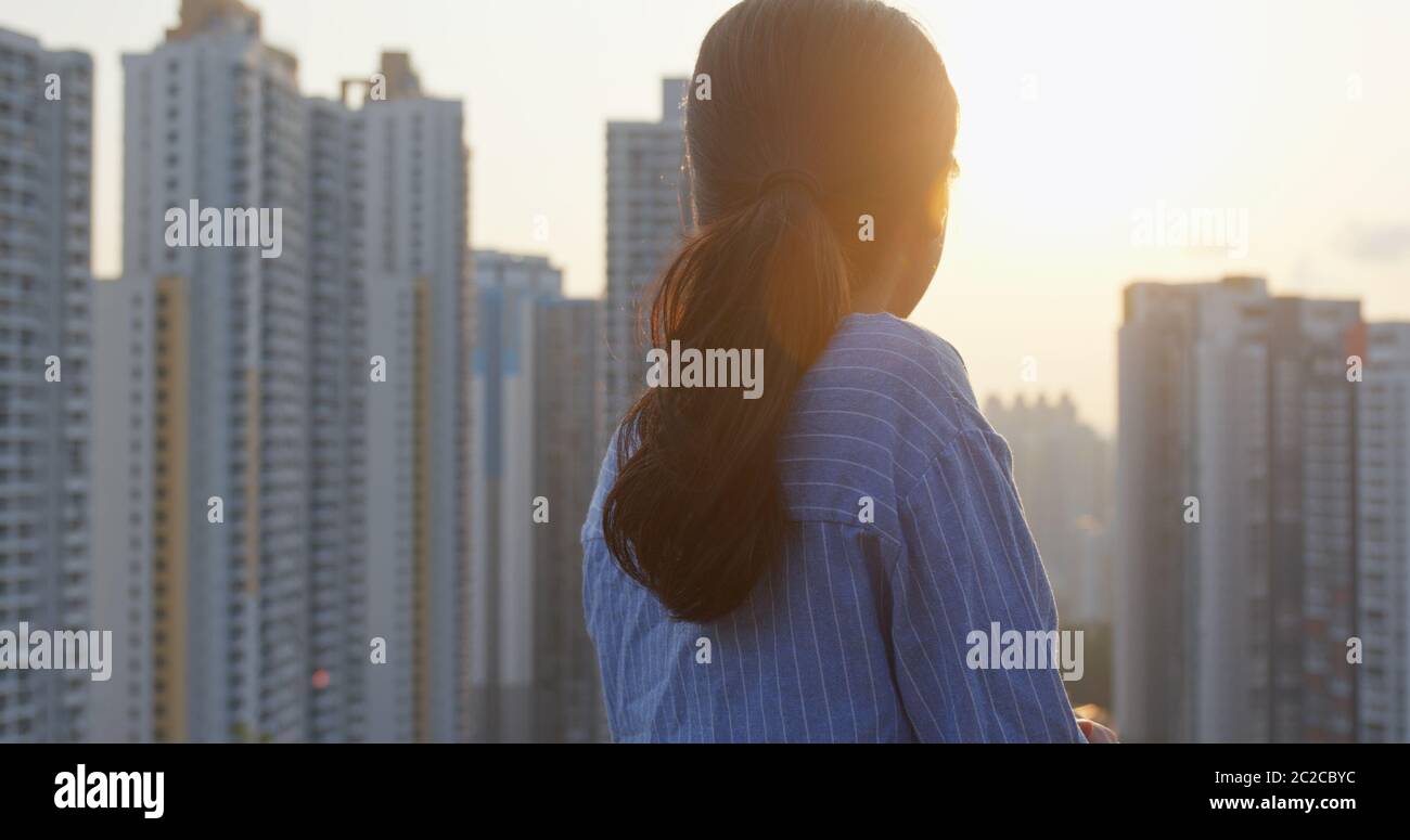 Donna guarda l'edificio in città e pensa al tramonto Foto Stock