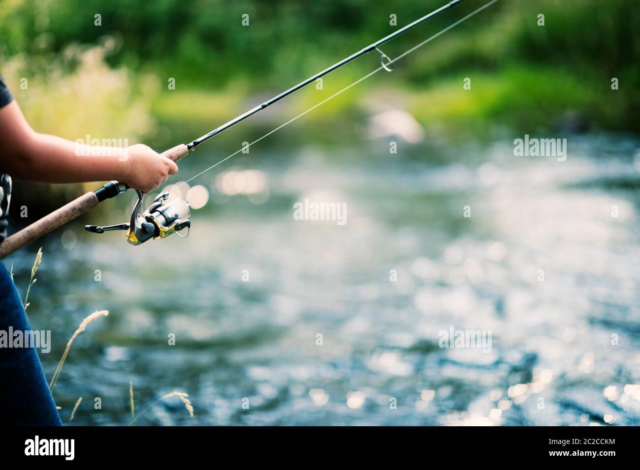 Canna da pesca e mulinello in mani sul fiume Foto Stock