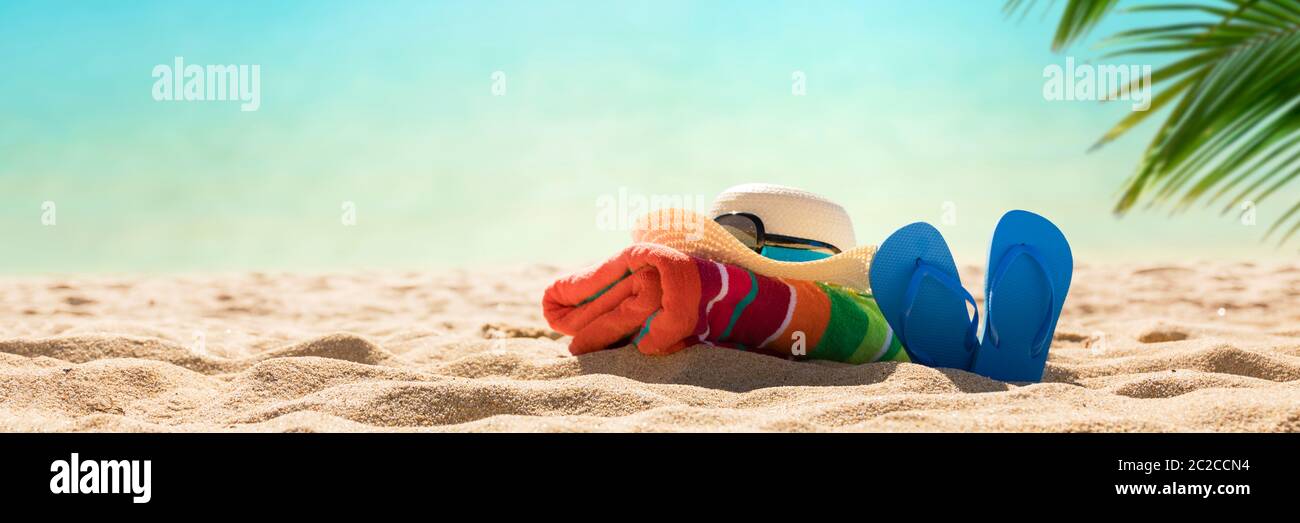 Accessori spiaggia cappello di paglia, infradito, asciugamano sulla soleggiata spiaggia tropicale, vacanze estive Foto Stock