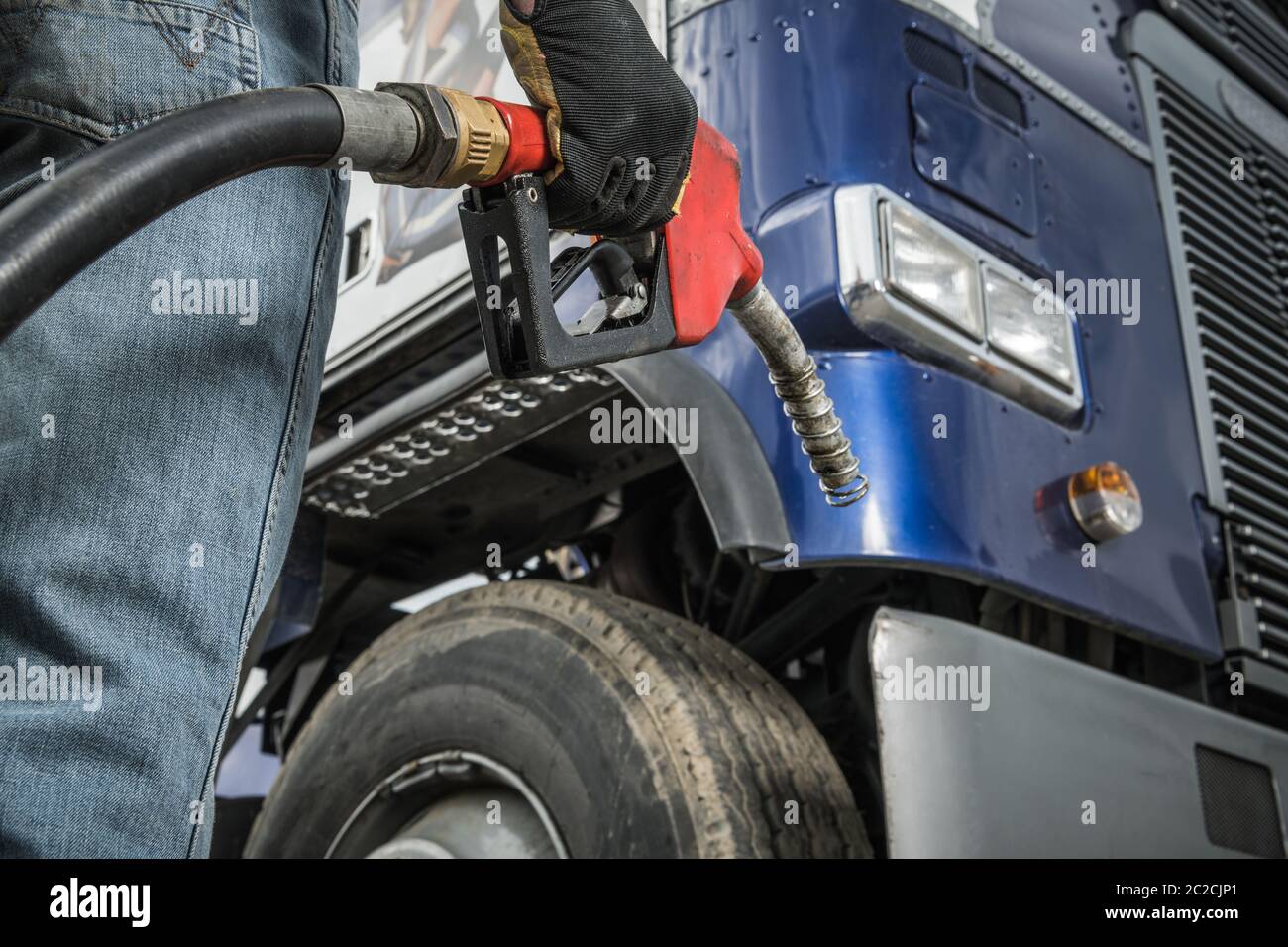 Trucker davanti al suo camion che si prepara per il rifornimento tenendo in mano l'ugello della pompa erogatrice diesel. Settore dei trasporti. Foto Stock