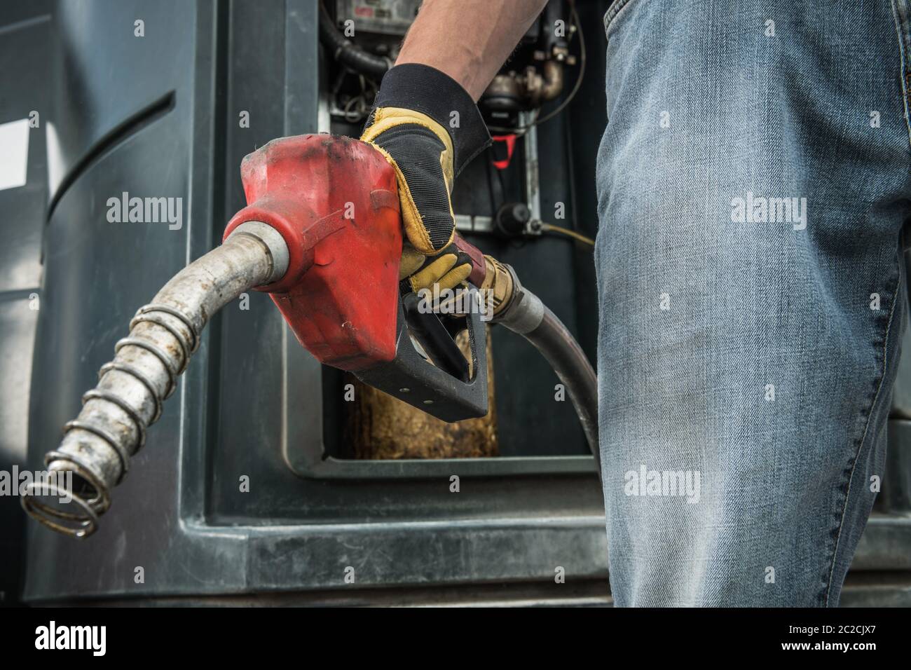 Tema industria dei trasporti. Trucker con la spazzola per pompa diesel in mano che si prepara a rifornire il suo semi-camion. Chiudi foto. Foto Stock