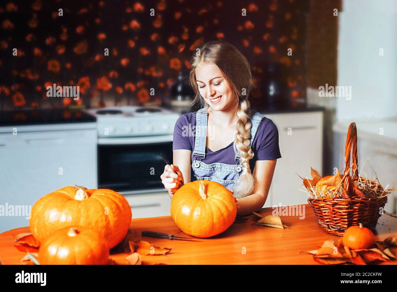 una bella donna bionda dipinge zucche per halloween a casa in cucina Foto Stock