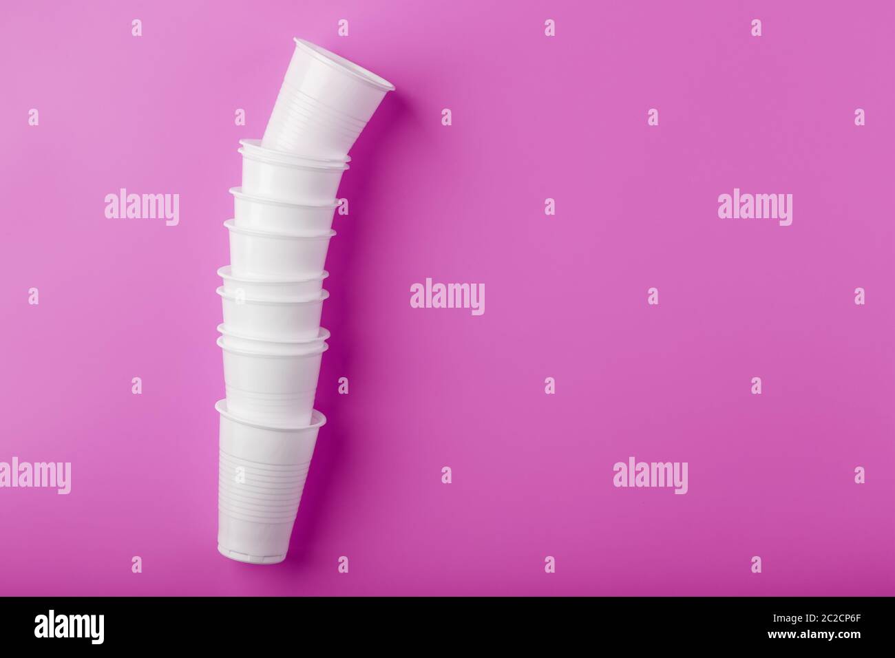 Bicchieri monouso in plastica bianca per stoviglie in fila, su sfondo rosa. Foto Stock