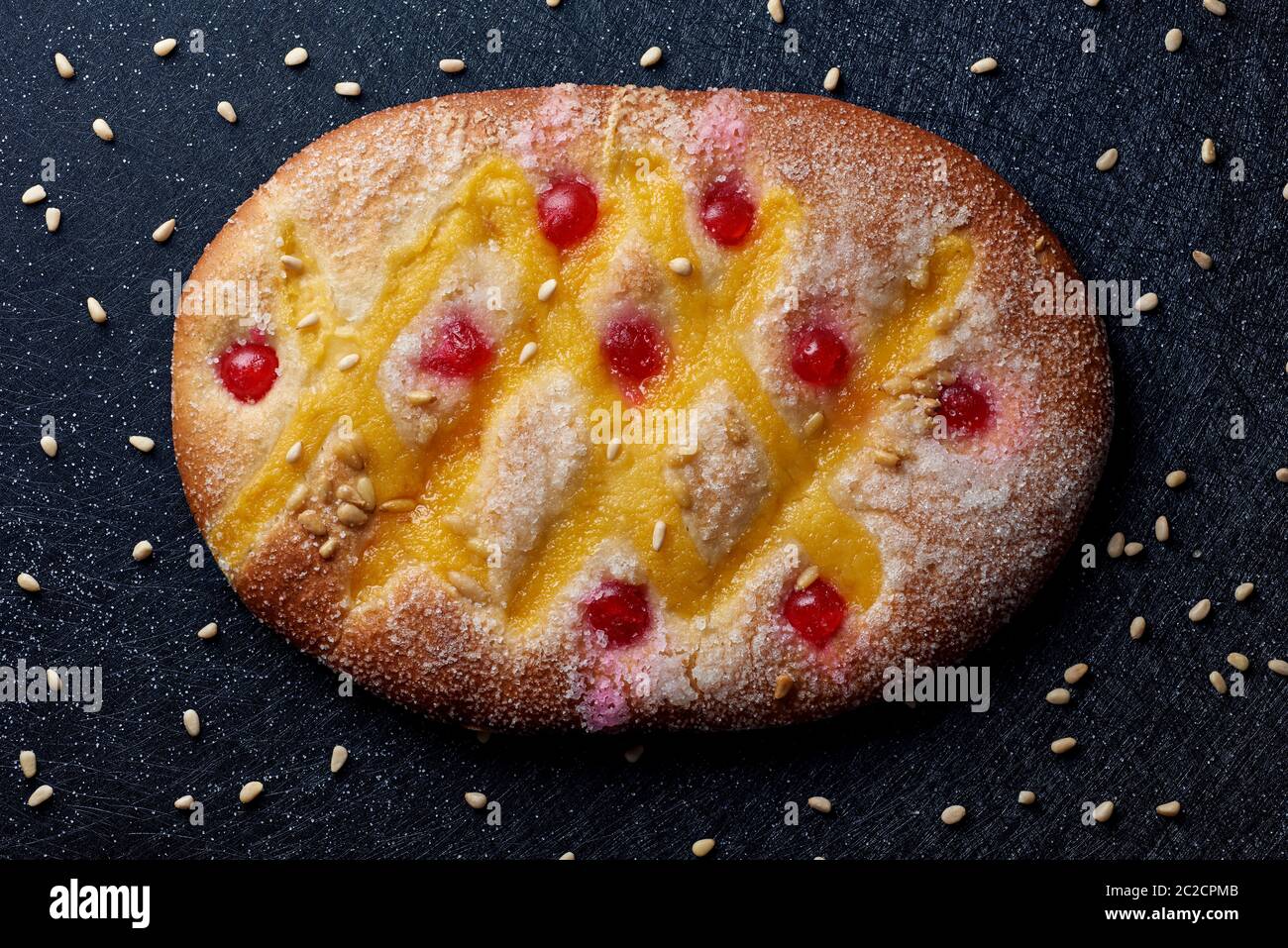 Vista ad alto angolo di una coca de Sant Joan, una tipica dolce torta piatta della Catalogna, Spagna, mangiata a San Giovanni, su una superficie di tessuto nero spruzzata Foto Stock