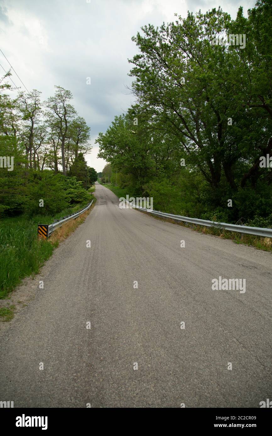 Prospettiva di strada di campagna con alberato fiancheggiata lati e guardrail. Foto Stock