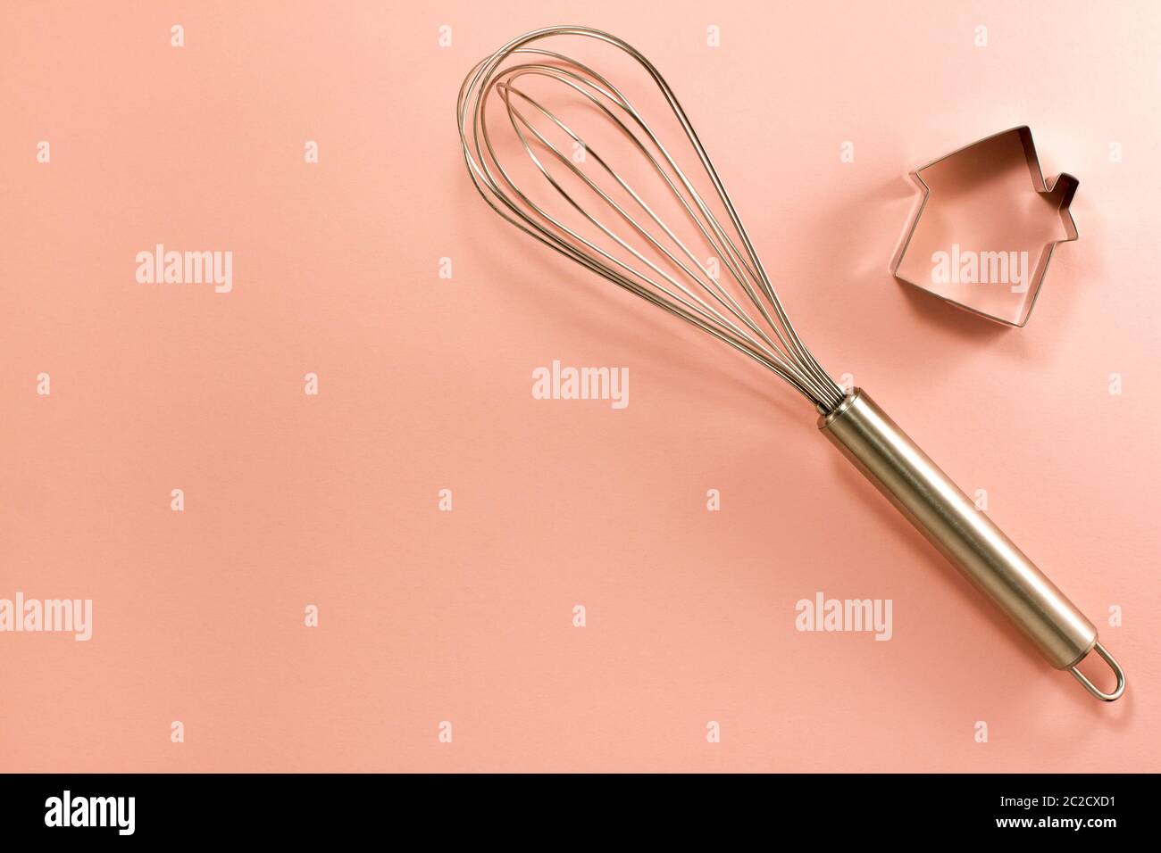 Frusta in acciaio e taglierina a forma di casa sulla destra dall'alto. Vista dall'alto in piano. Concetto di cucina dolciaria con spazio di copia su carta rosa brillante bac Foto Stock