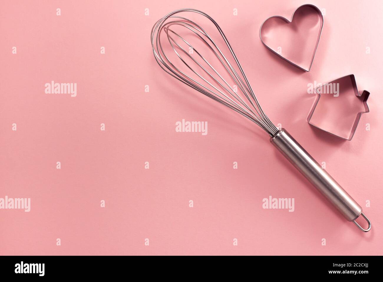 La frusta in acciaio e la taglierina a forma di cuore sulla destra dall'alto. Vista dall'alto in piano. Concetto di cucina dolciaria con spazio copia su un pap rosa brillante Foto Stock