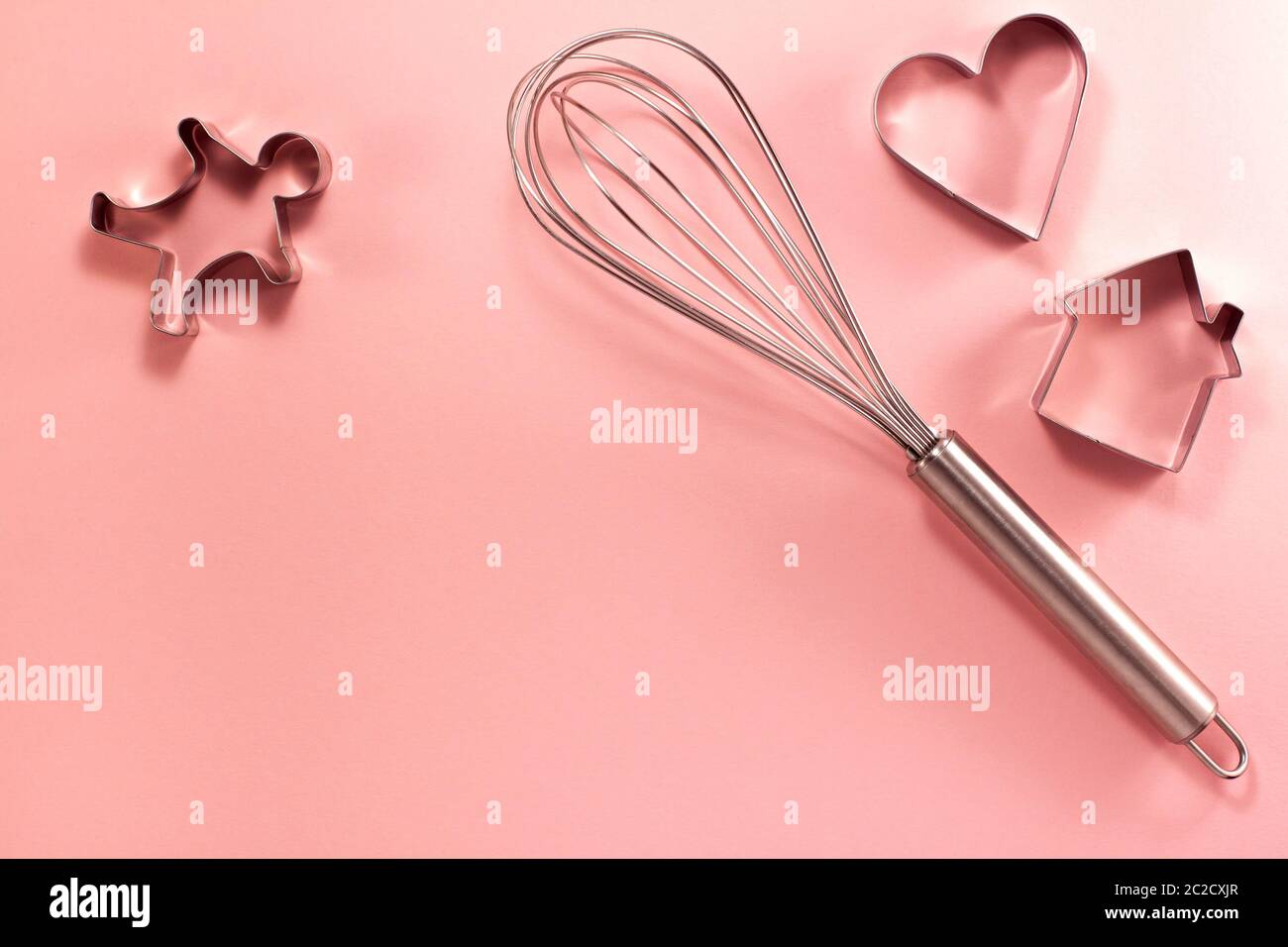 La frusta in acciaio ospita l'uomo e la taglierina a forma di cuore sulla destra dall'alto. Vista dall'alto in piano. Concetto di cucina dolciaria con spazio di copia su rosa brillante Foto Stock