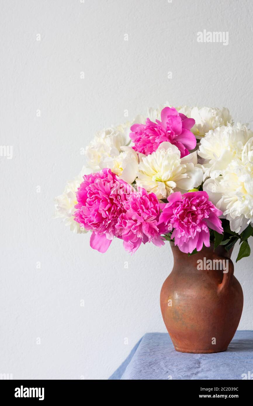 Bel bouquet di peonie in una pentola di argilla si erge su un tavolo con una tovaglia di lino blu Foto Stock