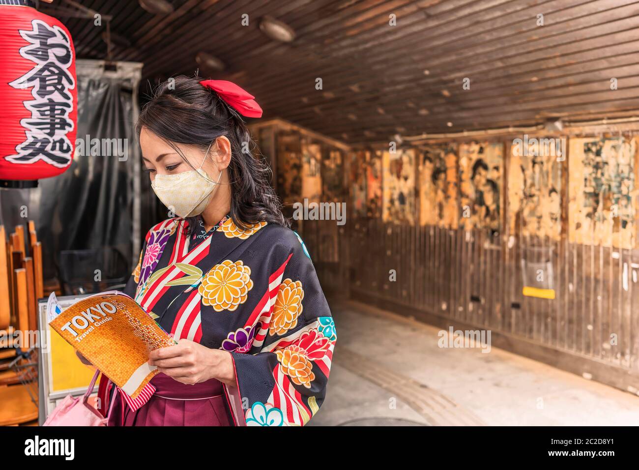 Donna giapponese in hakama kimono con una maschera di tessuto e leggendo una guida turistica della città di Tokyo al sottopassaggio del Concourse Yuraku decorato con un rosso Foto Stock