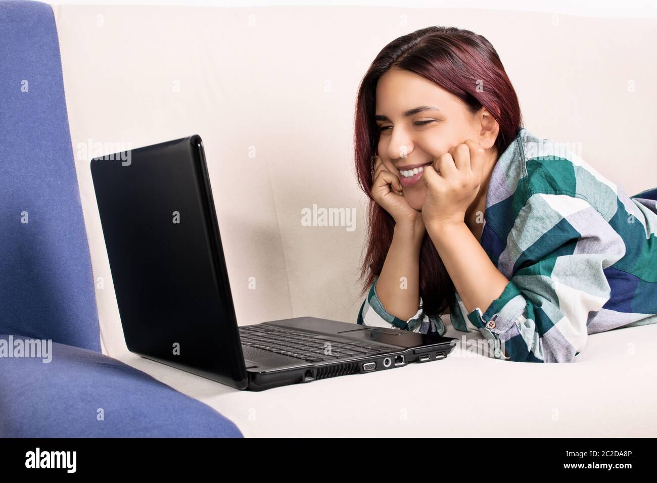Immagine ravvicinata di un bel sorriso ragazza a casa giacente sul suo lettino, guardando una schermata di un laptop. Sono contento quando parlo ai miei amici preferiti. Foto Stock
