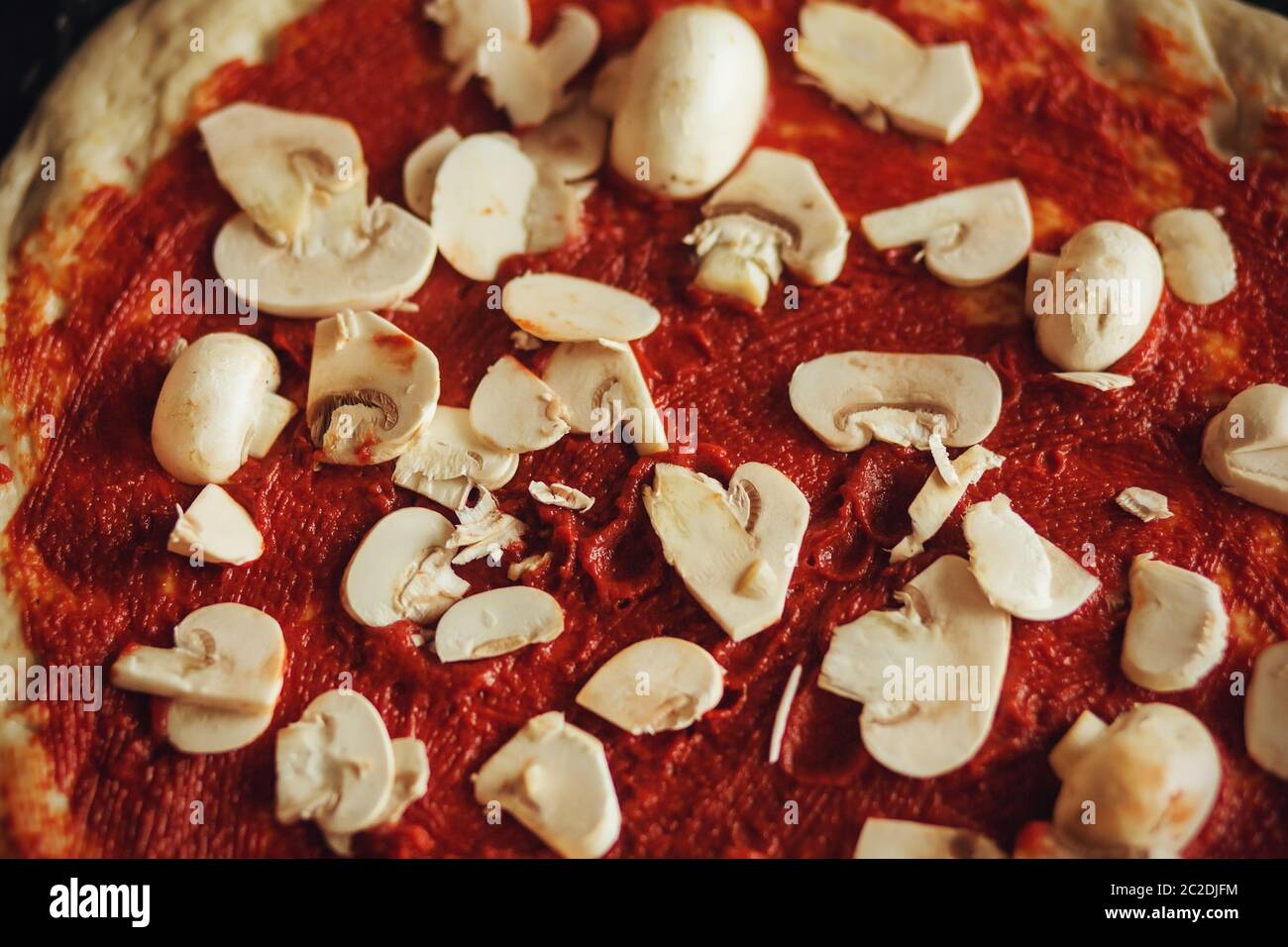 Pizza base - impasto spalmato con delizioso pomodoro in pasta e cosparso di funghi bianchi a fette. Il processo di cottura a casa. Foto Stock