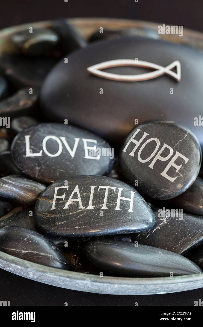 vita religiosa con sassi incisi con parole amore, fede, speranza e un simbolo cristiano di pesce sul retro Foto Stock