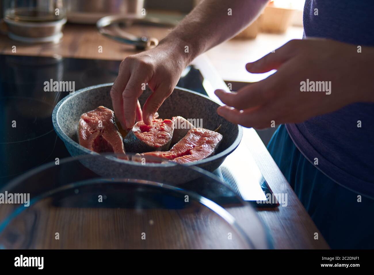 un uomo arrostiva il pesce in una padella sulla stufa Foto Stock