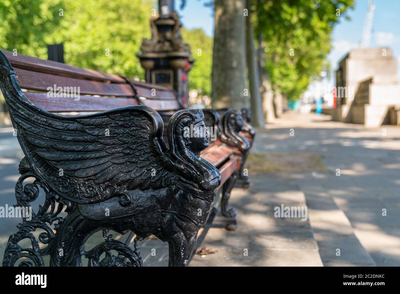 Panca in legno di ghisa sull'argine ornata con una testa di Sphinx alata nera che si affaccia maestosamente sul Tamigi a Londra, Inghilterra Foto Stock