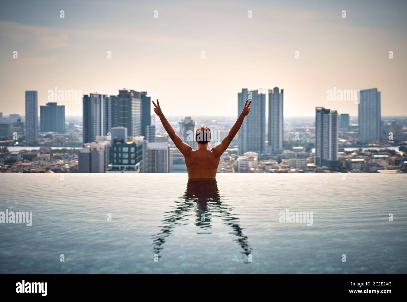Vista posteriore di felice libertà uomo con braccia rialzate godersi la sua vacanza estiva in piscina Foto Stock